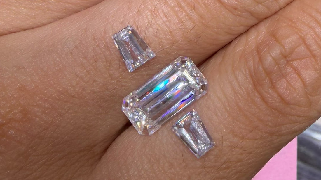 A 14 by 7.5 mm emerald cut moissanite on a hand with a matched pair of trapezoid side stones, arranged as a three stone ring