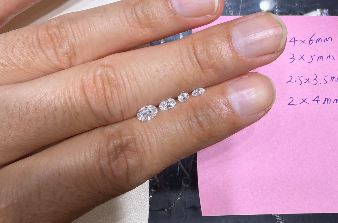 Four oval moissanite samples lined up on one finger, beside the handwritten list of their sizes