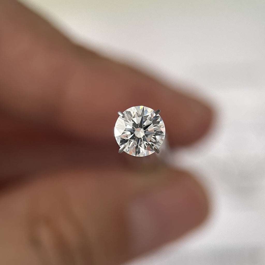 Round hearts and arrows moissanite loose stone held in tweezers - Caratura