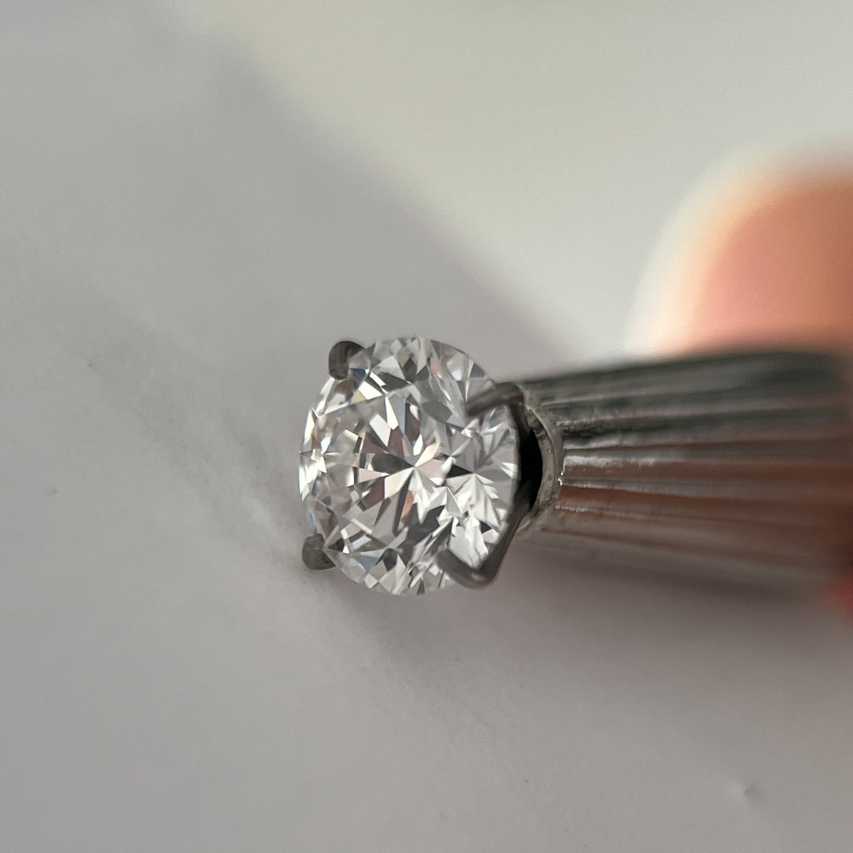 Round moissanite loose stone in tweezers showing brilliance - Caratura